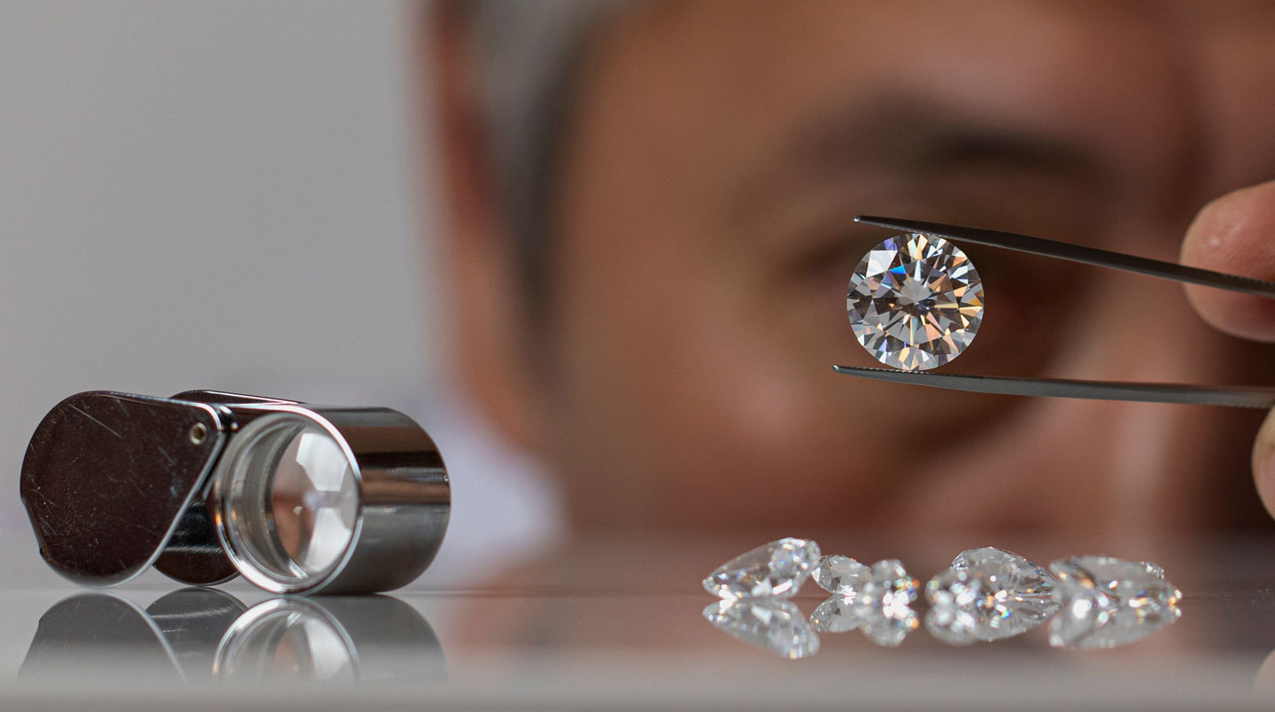 Créatrice de bijoux vue de profil en train de comparer deux pierres fines à contre-jour devant une fenêtre dans un atelier moderne épuré, concentration sur le geste professionnel